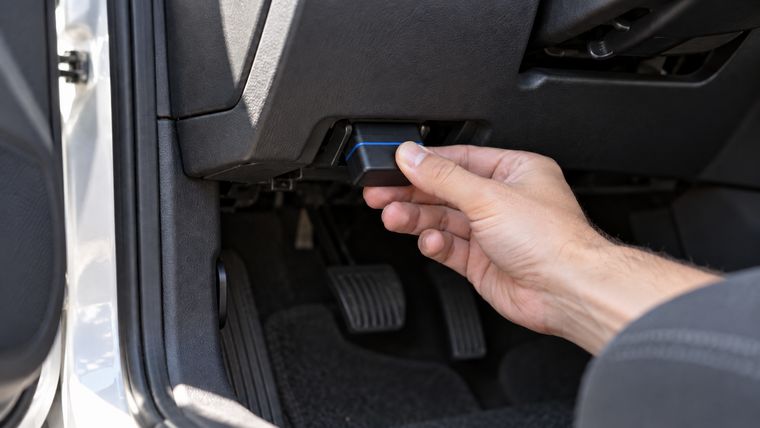 Adaptador de diagnóstico sendo encaixado na tomada embaixo do painel do carro.